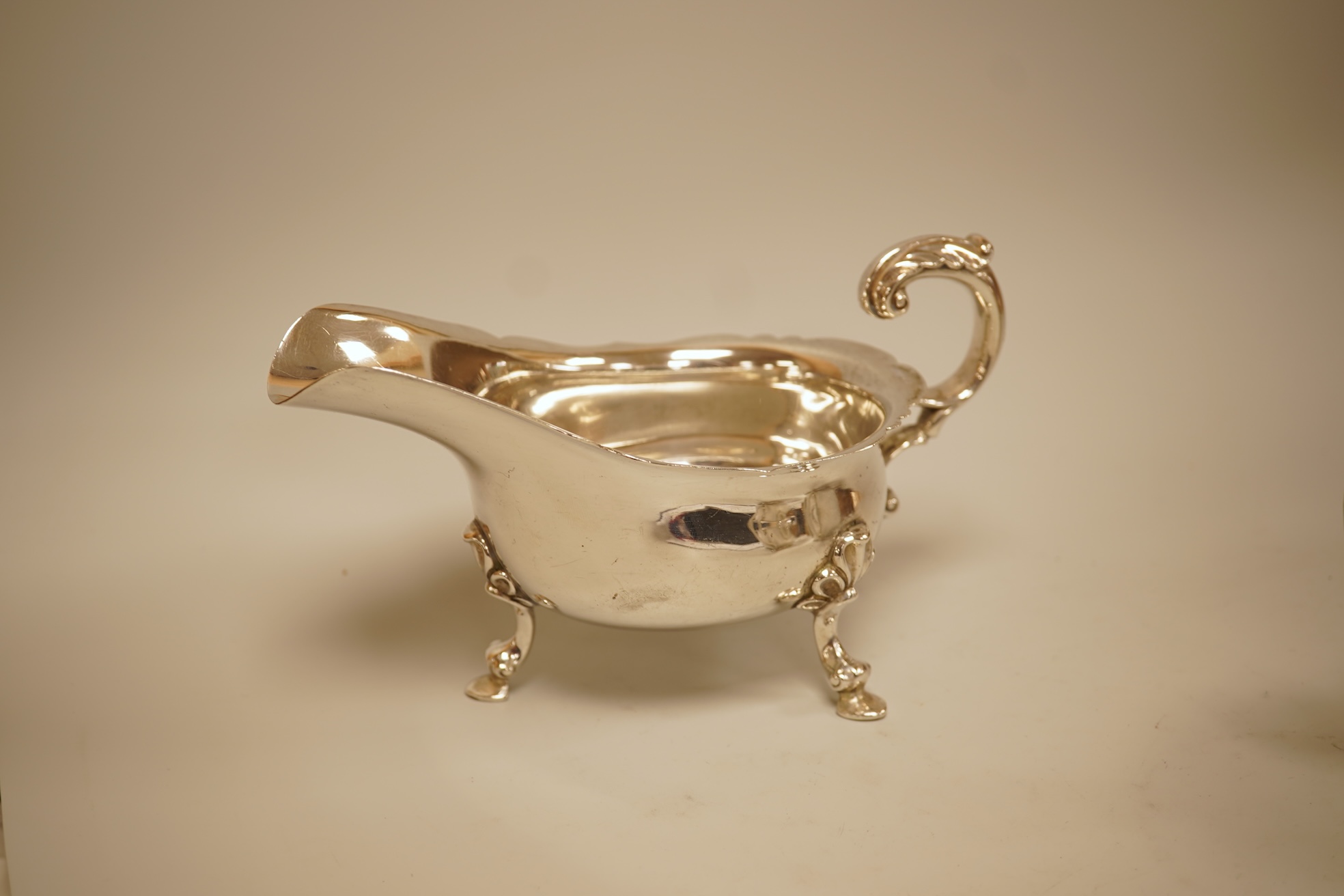 A pair of George V silver sauceboats by Walker & Hall, Sheffield, 1929/30, length 17.9cm together with a George V silver sauceboat with flying scroll handle, William Comyns & Sons Ltd, London 1926, 16.4oz.